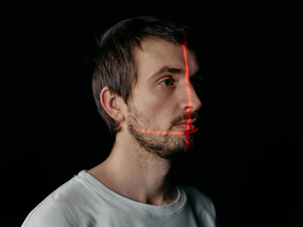 Portret van een man in profiel tegen een zwarte achtergrond, terwijl rode laserlijnen van een 3D-scanner over zijn gezicht schijnen.