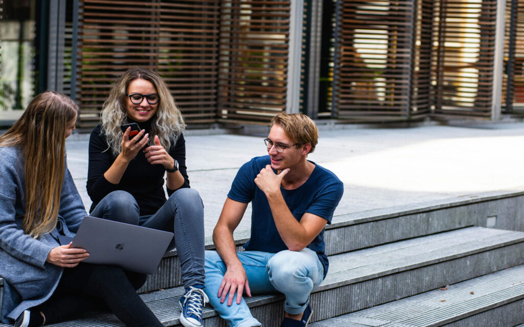 Twee vrouwen en een man zitten op een trap met elkaar in gesprek