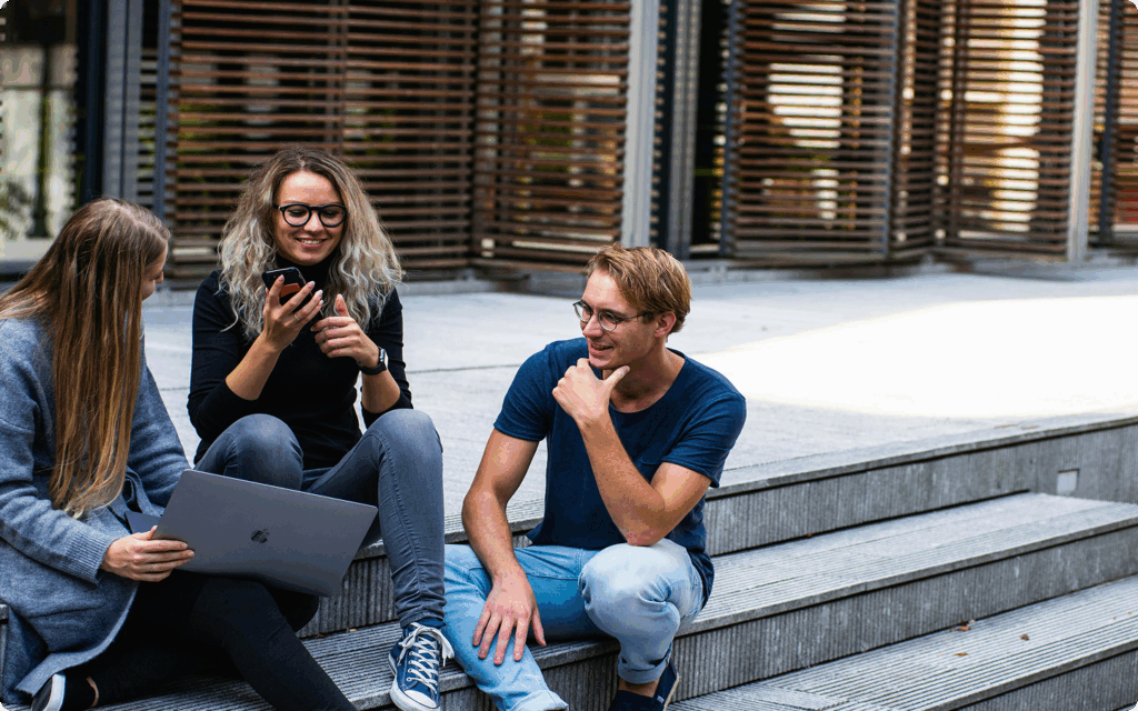 Twee vrouwen en een man zitten op een trap met elkaar in gesprek