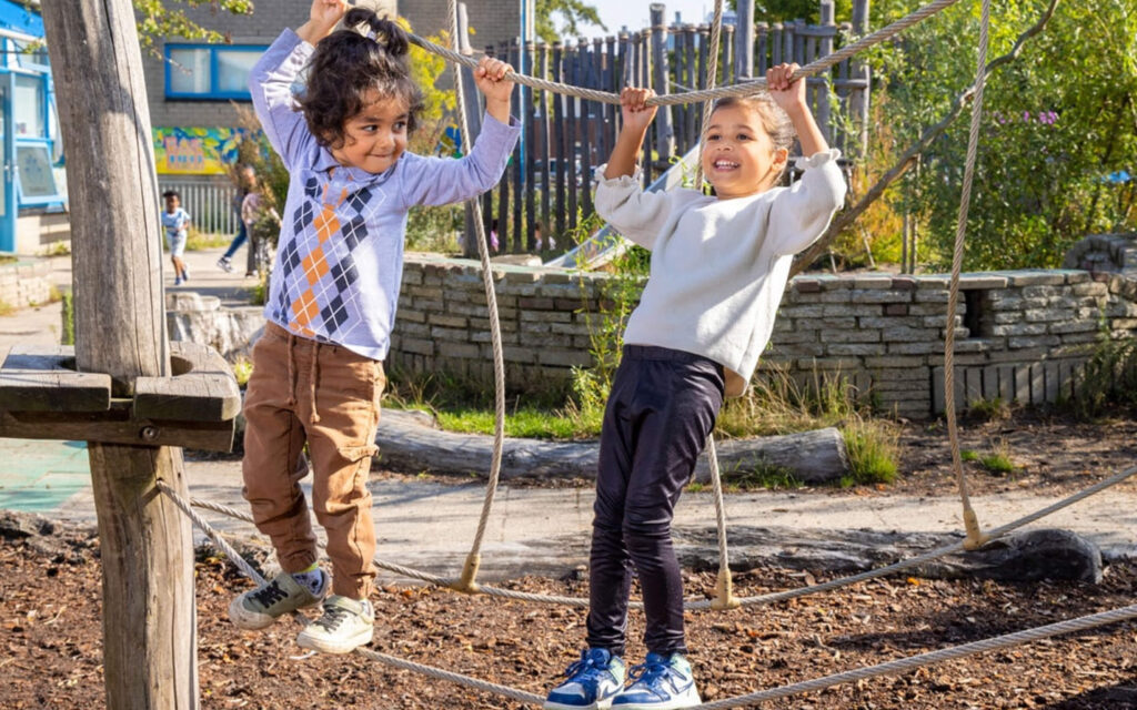 Twee jonge kinderen spelen vrolijk op een touwklimparcours op een uitdagend ingericht schoolplein.