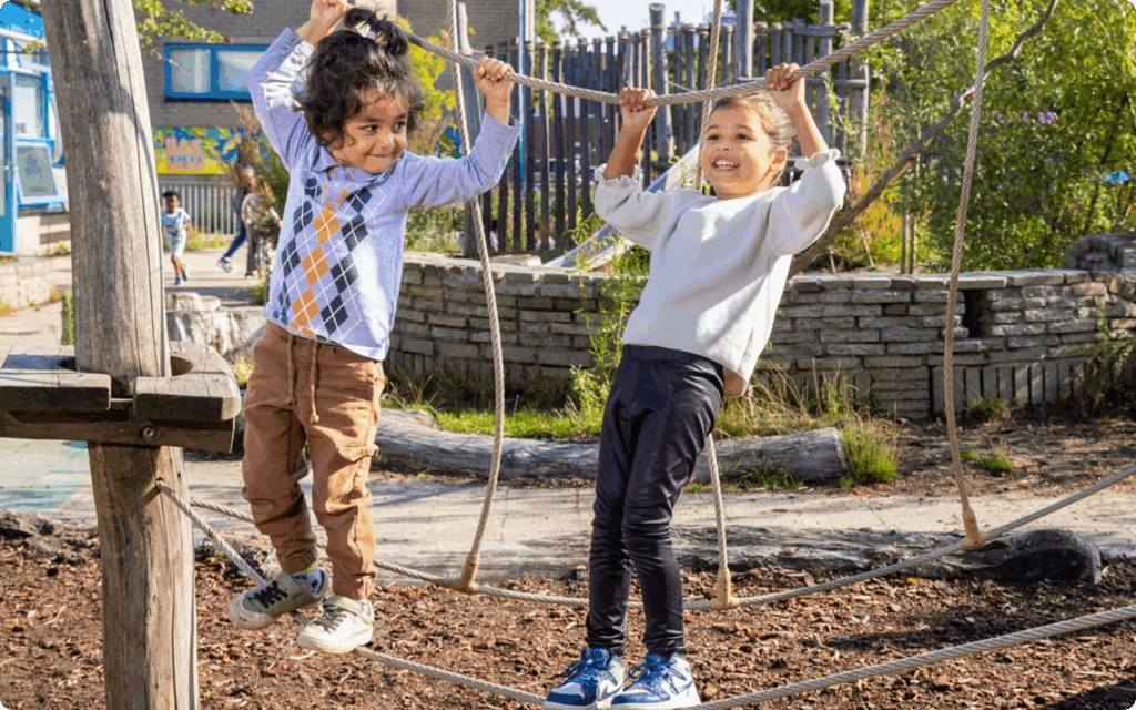 Twee jonge kinderen spelen vrolijk op een touwklimparcours op een uitdagend ingericht schoolplein.