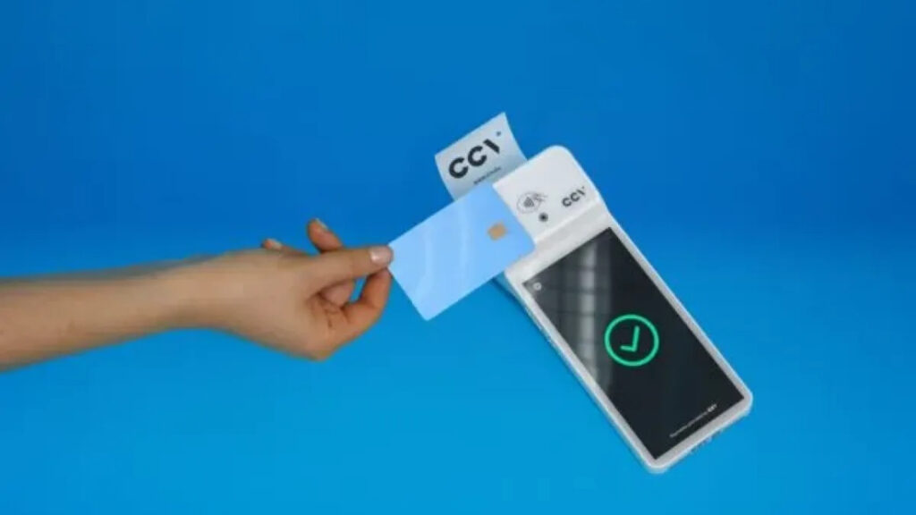 Een close-up van een hand die een blauwe betaalpas contactloos tegen een witte CCV-betaalterminal houdt. Op het scherm van de terminal verschijnt een groene cirkel met een vinkje tegen een blauwe achtergrond.