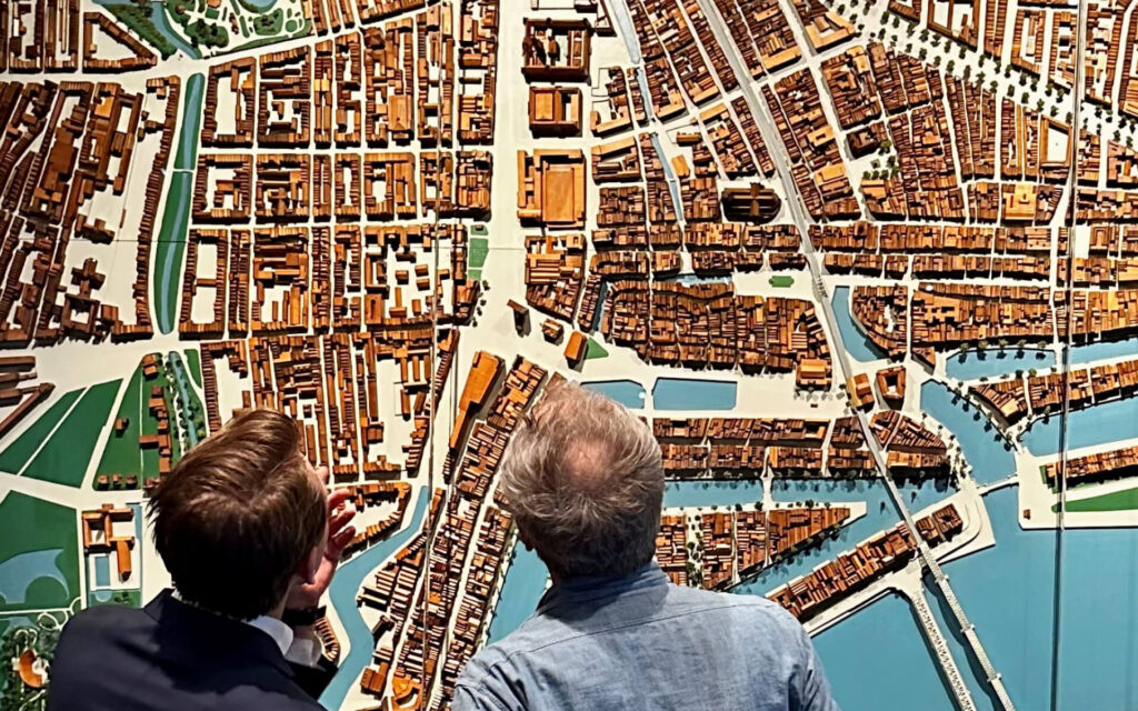 Twee mannen van achteren gezien die naar een gedetailleerd stadsmodel van Rotterdam kijken.