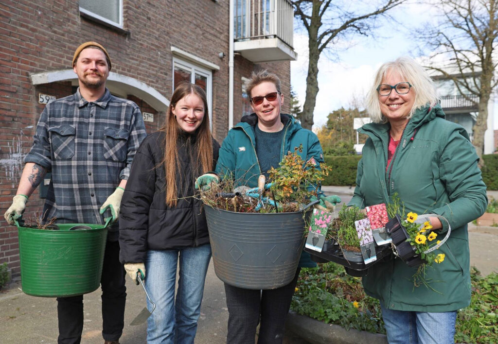 Een groep van vier buren staat op straat met tuingereedschap en nieuwe planten.