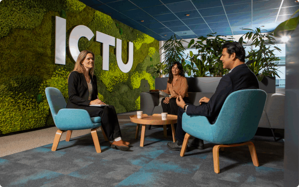 Drie personen in een informele vergaderhoek met een groen mosmuur en het grote ICTU-logo.