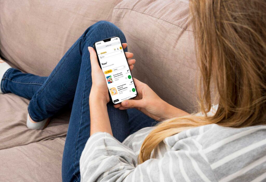 Vrouw ligt op de bank en doet boodschappen via de Jumbo website op haar telefoon