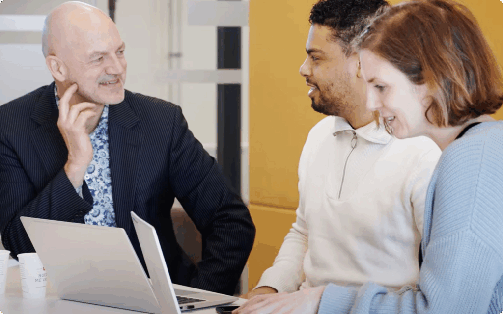 Drie collega's zitten samen, kijken naar een laptop en voeren een overleg in een kantooromgeving.