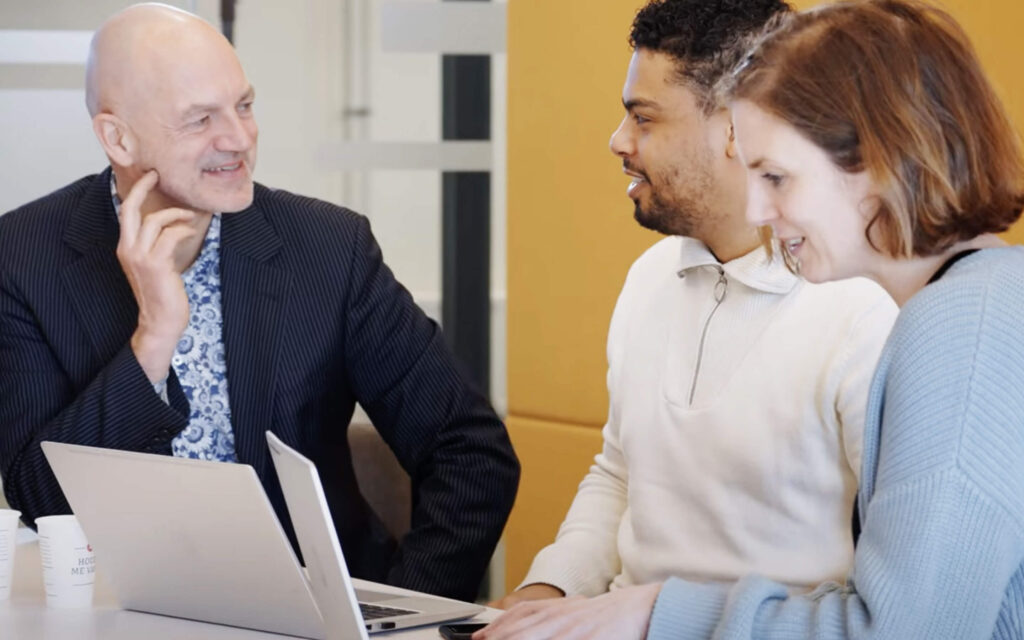 Drie collega's zitten samen, kijken naar een laptop en voeren een overleg in een kantooromgeving.