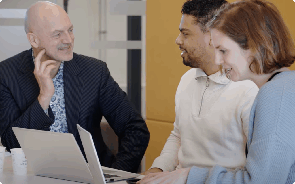 Drie collega's zitten samen, kijken naar een laptop en voeren een overleg in een kantooromgeving.