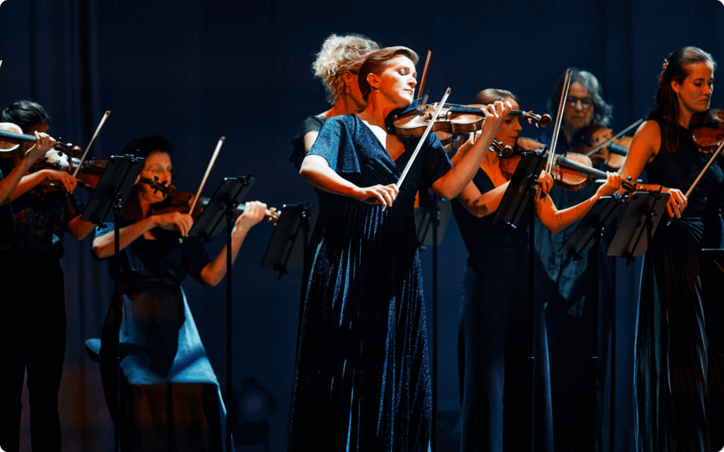 Vrouwelijke musici van het orkest spelen viool in donkerblauwe jurken op een podium met zachte belichting.