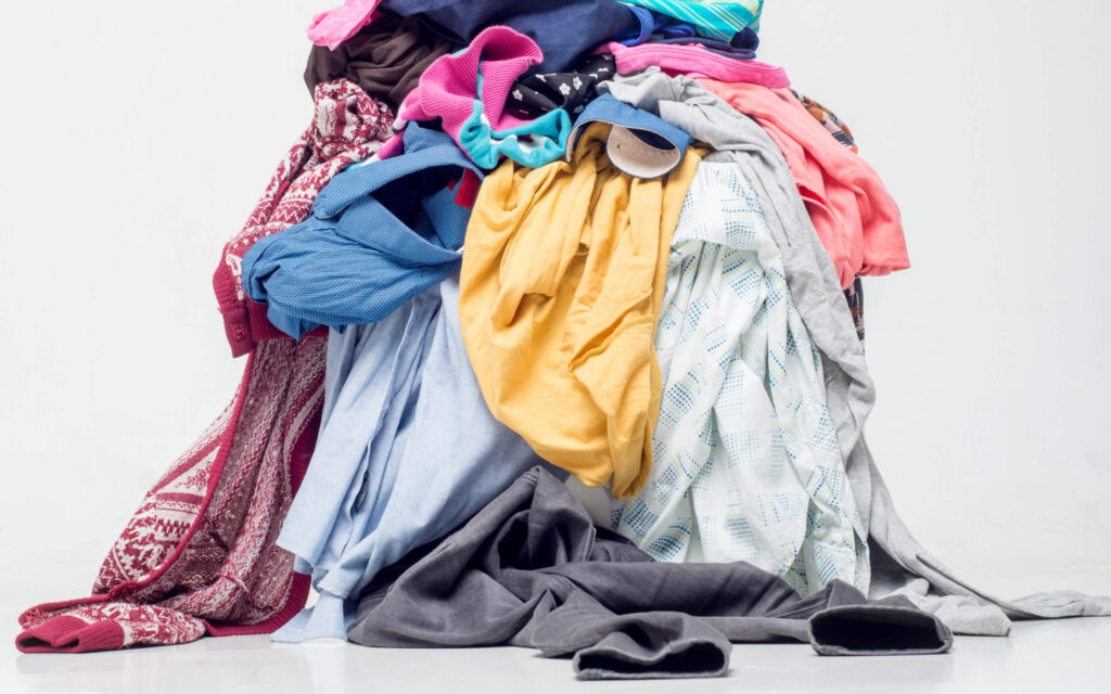 Grote, kleurrijke stapel gebruikte kleding en textiel op een witte achtergrond.