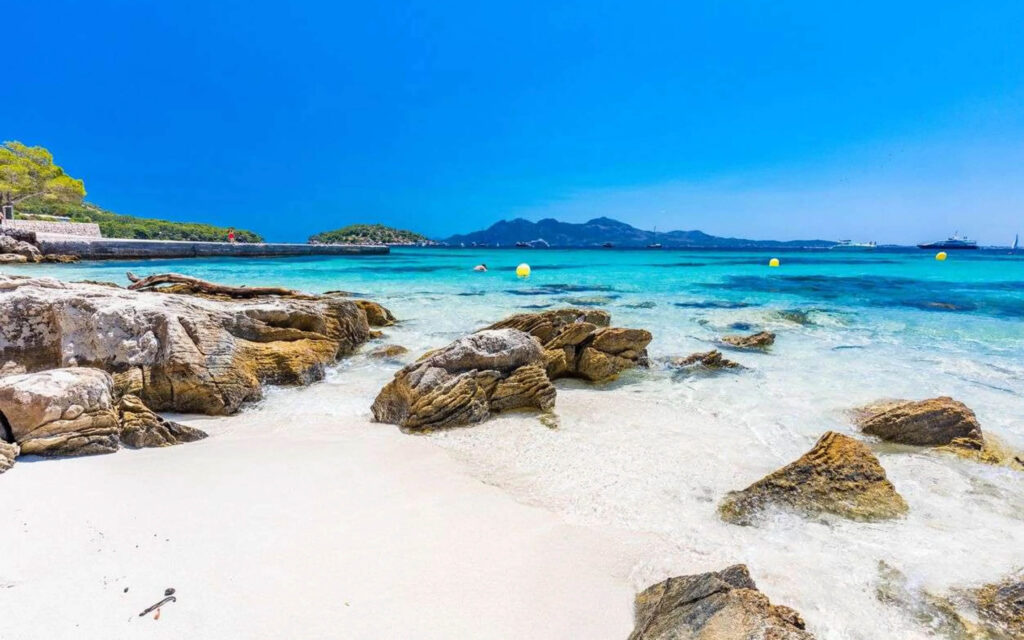 Idyllisch, zonnig strand met turquoise water, witte rotsen en wit zand onder een strakblauwe lucht.