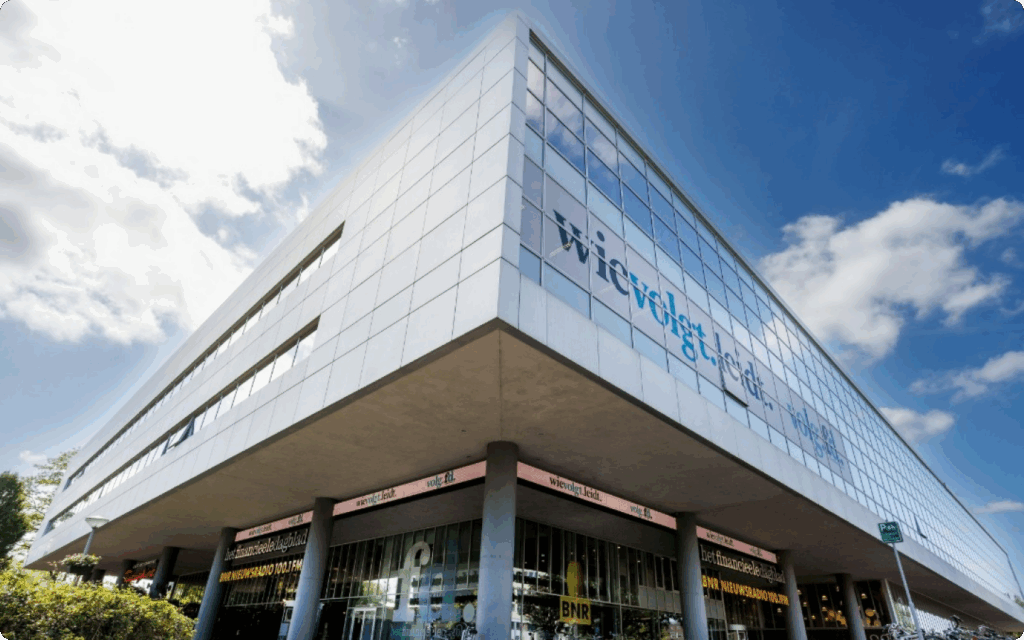 Architecturale, hoekige opname van het moderne FD Mediagroep gebouw onder een blauwe lucht, met logo's op de ramen.