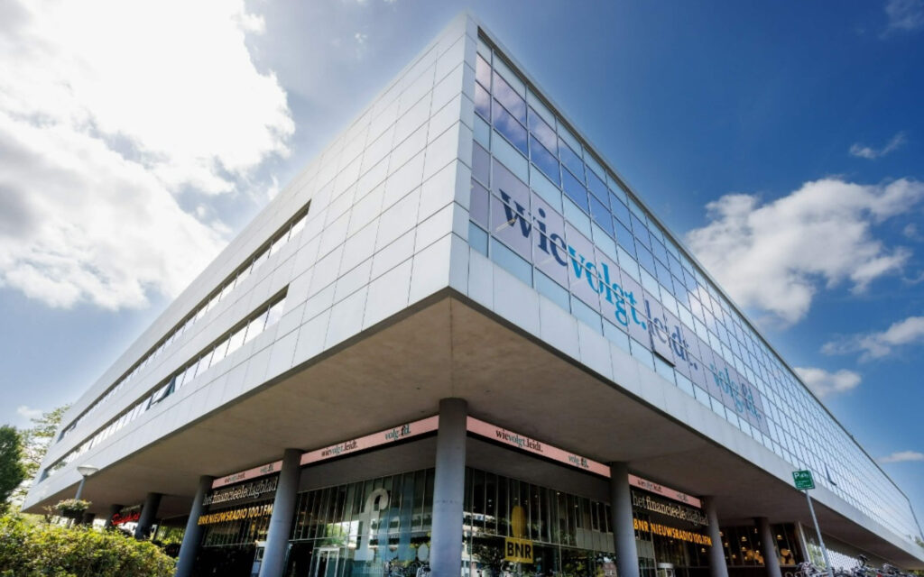 Architecturale, hoekige opname van het moderne FD Mediagroep gebouw onder een blauwe lucht, met logo's op de ramen.