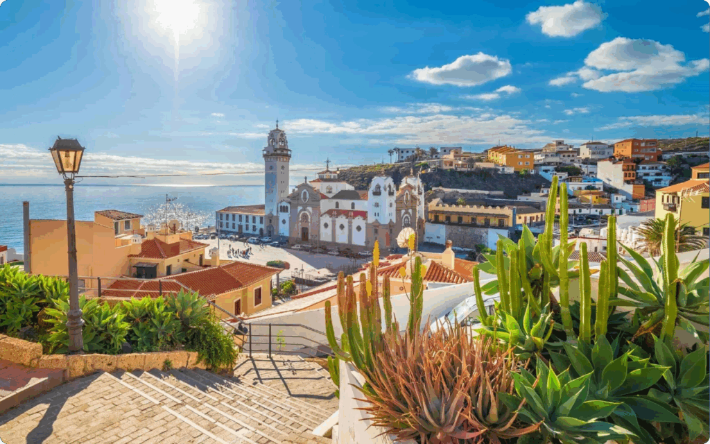 Panoramisch uitzicht op een zonnig mediterraan/Canarisch kuststadje met een witte kerk en helderblauwe lucht.