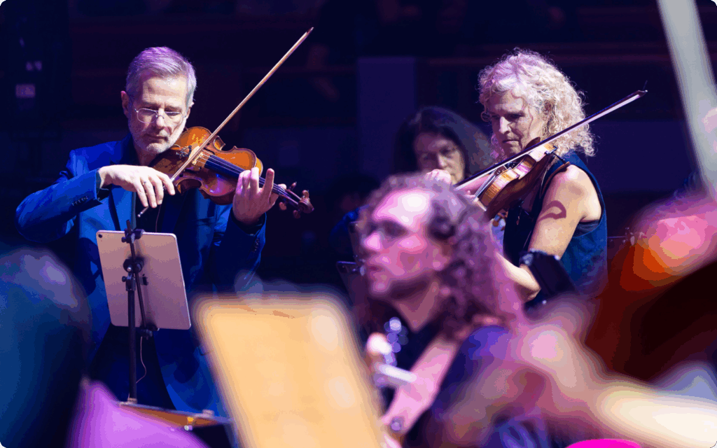 Close-up van musici die viool spelen op het podium, waarbij één muzikant digitale bladmuziek gebruikt op een iPad.