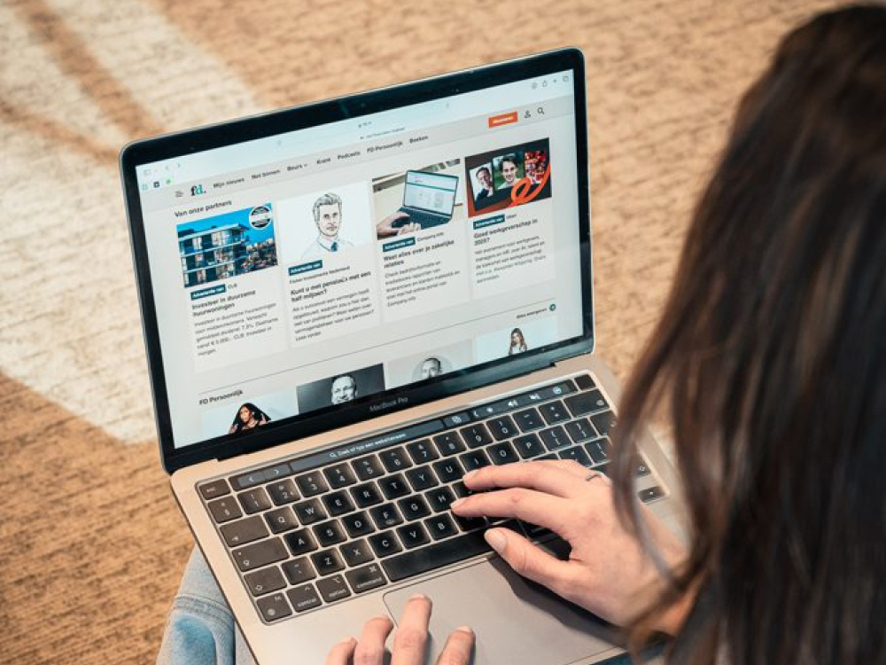 Persoon typt op een MacBook en bekijkt de nieuwspagina van Het Financieele Dagblad met diverse artikelen.