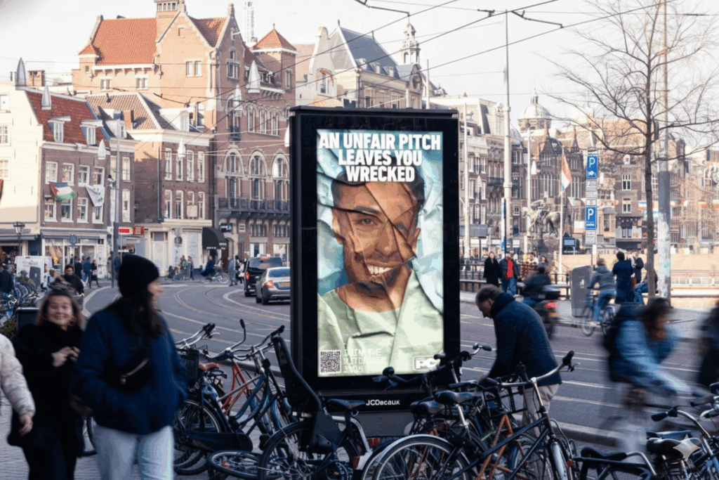 Campagne poster pitchcode in een straat in Amsterdam met veel fietsen.