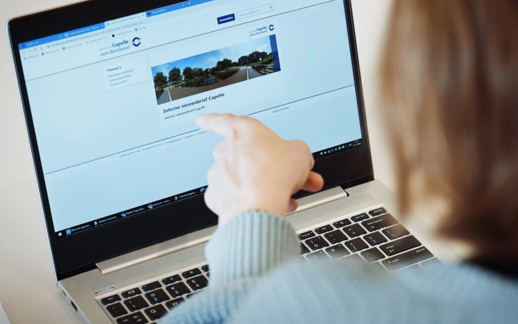 Vrouw wijst met haar vinger naar het scherm van een laptop, waar een interne nieuwsbrief van 'Capelle aan den IJssel' getoond wordt.