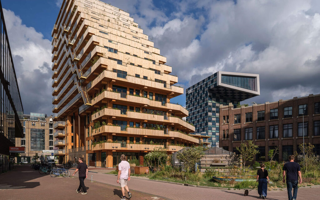 Het houten woongebouw SAWA in Rotterdam met groene terrassen, met op de achtergrond het STC-gebouw onder een bewolkte lucht.