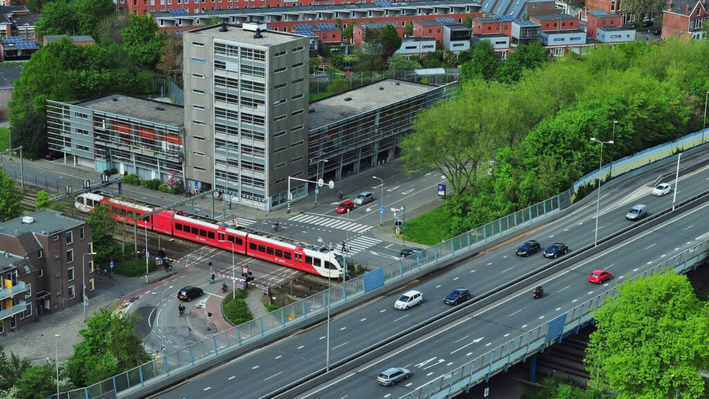 Luchtfoto van een verkeersknooppunt met een autoweg op een viaduct die een spoorweg met een rood-witte trein kruist.