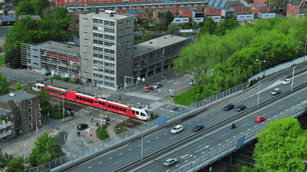 Luchtfoto van een verkeersknooppunt met een autoweg op een viaduct die een spoorweg met een rood-witte trein kruist.
