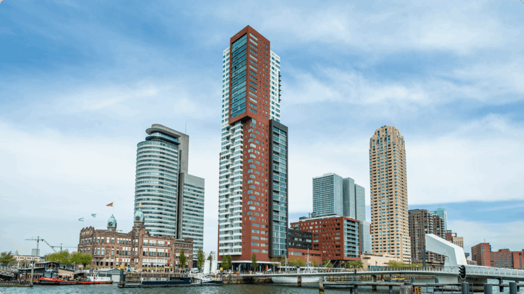 Een stadsgezicht vanaf het water met diverse moderne woontorens en het historische Hotel New York aan de kade.