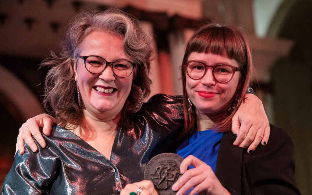 Eeva Liukku en uitgever Hilde Westerink glimlachen breed terwijl zij samen de Laurenspenning vasthouden.