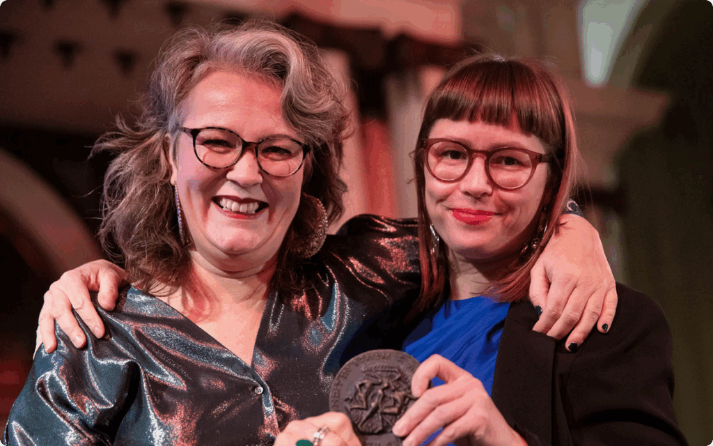 Eeva Liukku en uitgever Hilde Westerink glimlachen breed terwijl zij samen de Laurenspenning vasthouden.