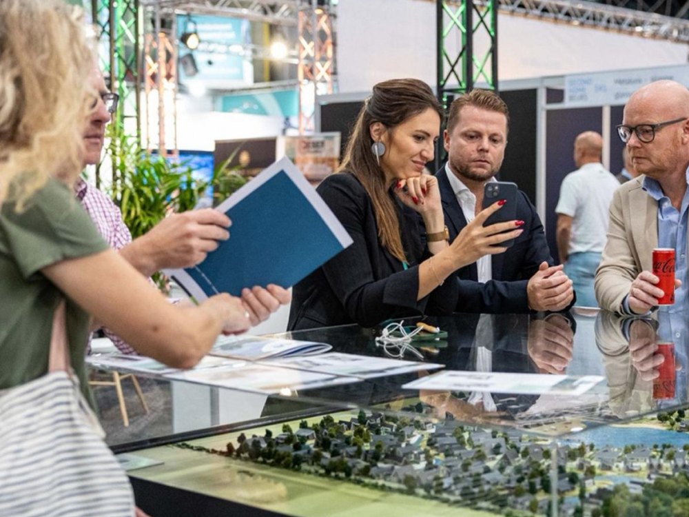 Bezoekers en exposanten in gesprek bij een maquette van een vakantiepark op de Second Home Beurs.