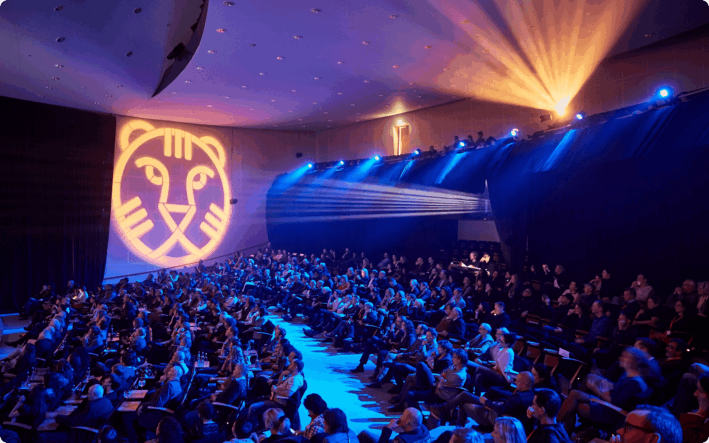 Een grote bioscoopzaal gevuld met publiek, verlicht door blauwe sfeerverlichting en een projectie van de IFFR-tijger op de zijwand.