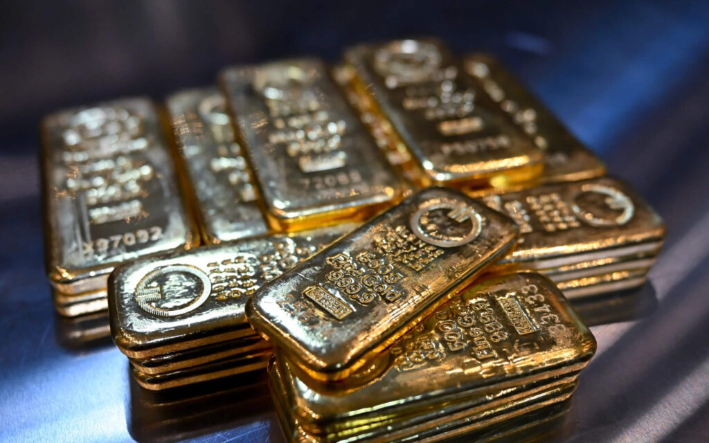 Een stapel glimmende goudstaven van 500 gram met officiële stempels, liggend op een reflecterend oppervlak.