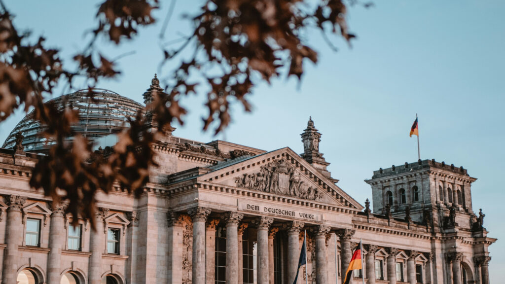 Het Reichstag-gebouw in Berlijn met de Duitse vlag en herfstbladeren op de voorgrond.
