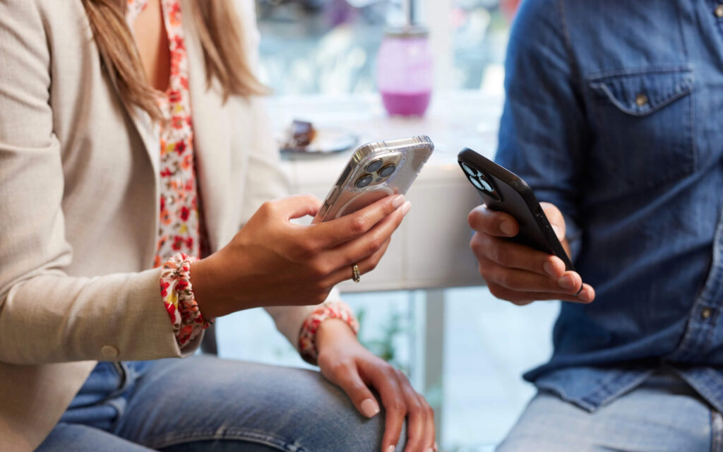 Close-up van twee personen die elk hun eigen smartphone vasthouden aan een tafel in een café.