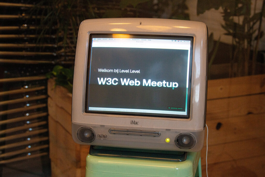 Een oude Apple iMac met beeldbuis, op het scherm staat "Welkom bij Level Level W3C Web Meetup".