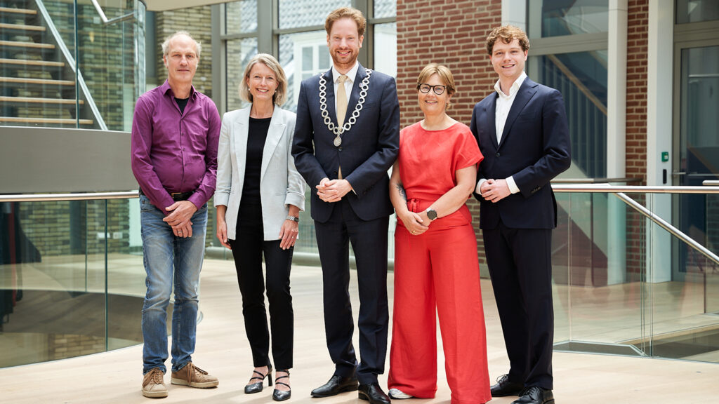 Groepsfoto van het college van burgemeester en wethouders in een modern gebouw.
