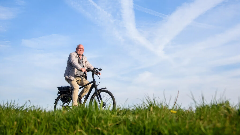 Een man fietst op een e-bike over een dijk tegen een blauwe lucht met lichte bewolking.