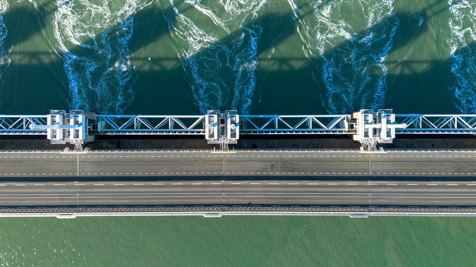 Een luchtfoto van de Oosterscheldekering met geopende schuiven en stromend water.