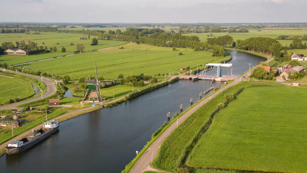 Luchtfoto van een kanaal met molen, ophaalbrug en vrachtschip.
